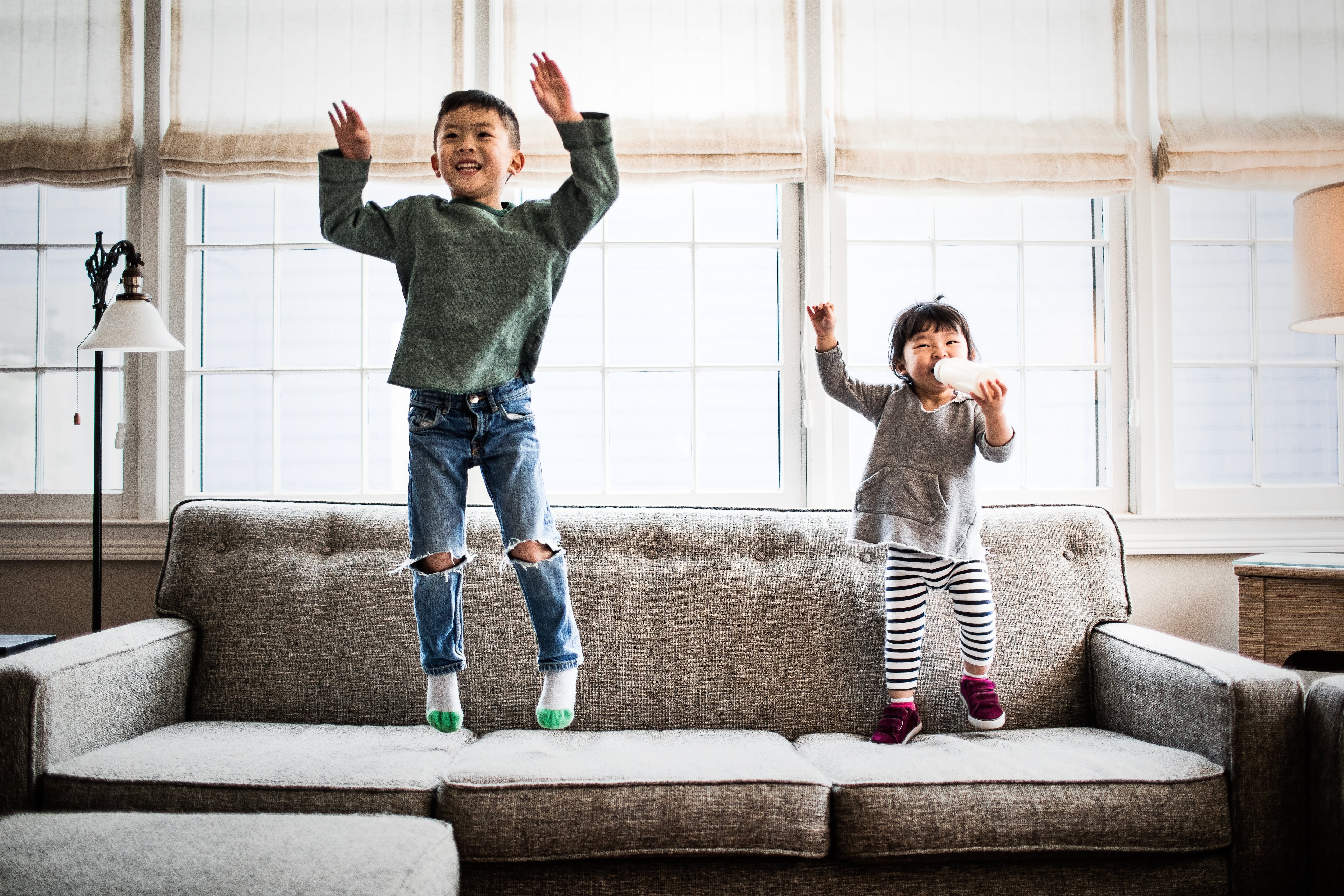 Young boy and baby girl jumping on the couch in excitement