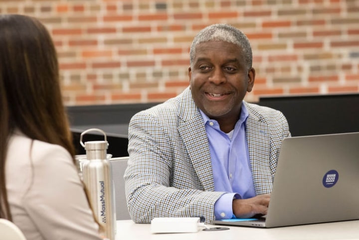 A business man with a laptop in front of him, conversing with a woman, while sitting at a table