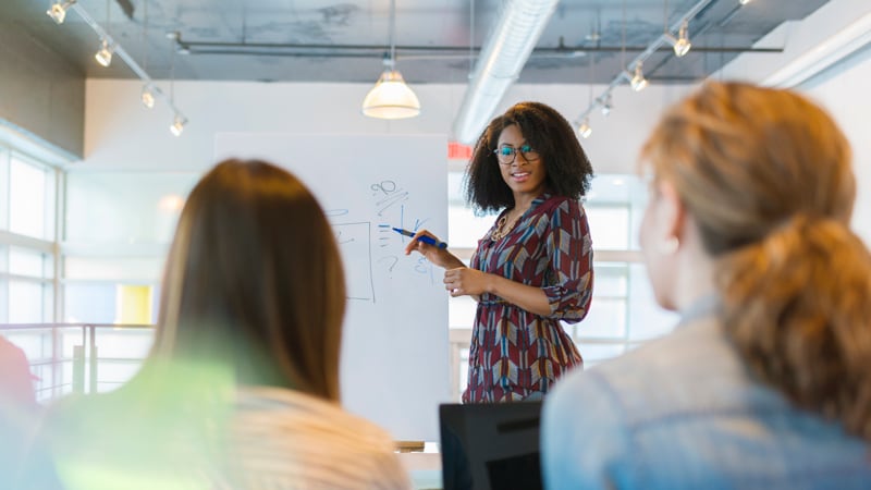 Businesswoman at whiteboard facing two seated coworkers