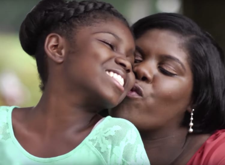 A mother kissing her young daughter's cheek while daughter smiles