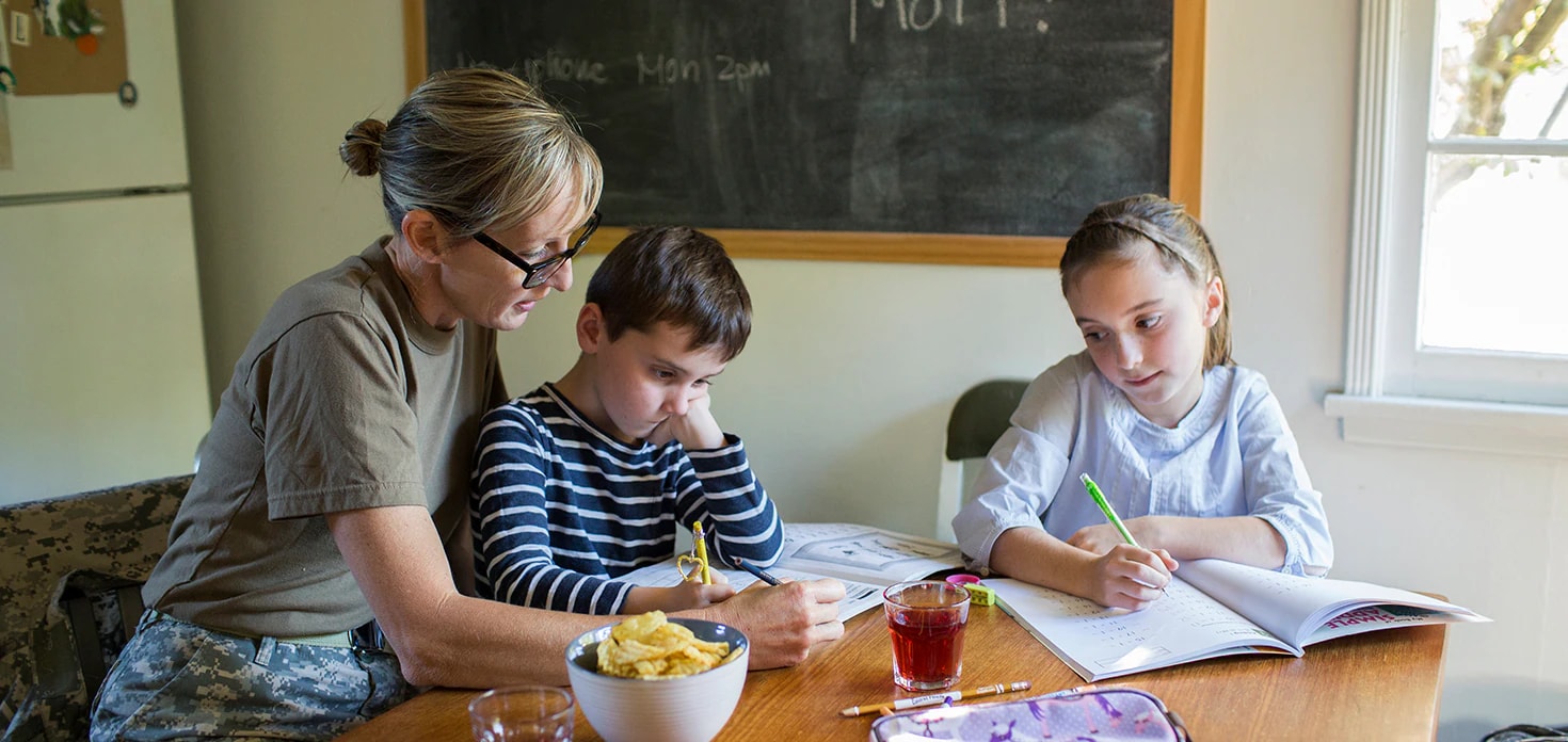 Mother in military uniform helping two kids at kitchen table with their homework.