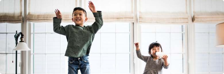 Two children jumping on couch with arms raised