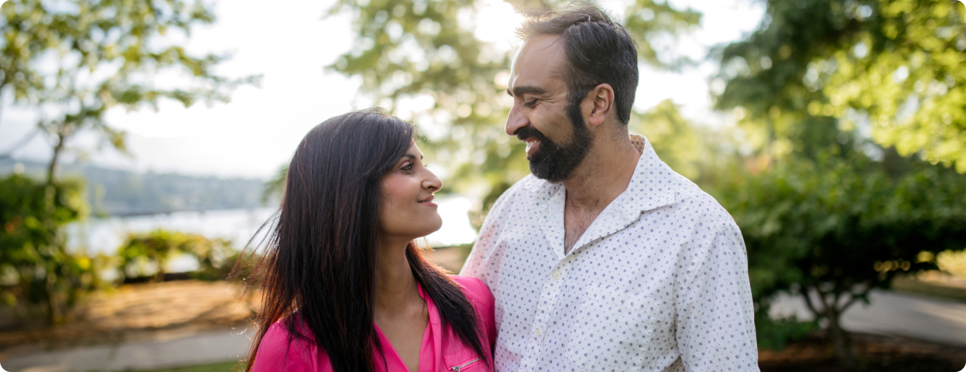 A man and a woman, walking in a park next to a lake, looking at each other and smiling