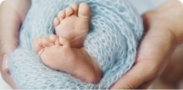 parent holding a baby wrapped in a blue blanket with feet pointing at camera