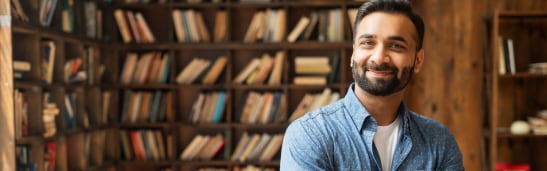 Man smiling at camera standing in front of bookshelf full of books
