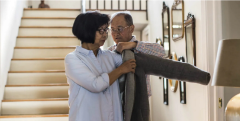 A man helping a woman put her coat on while standing in front of stairs