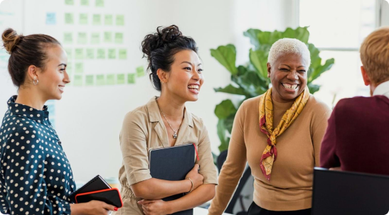 three females one wearing a polka dot top are all laughing with other employee wearing a burgundy top and has short blonde hair