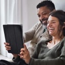 A man and a woman laughing while looking at a tablet