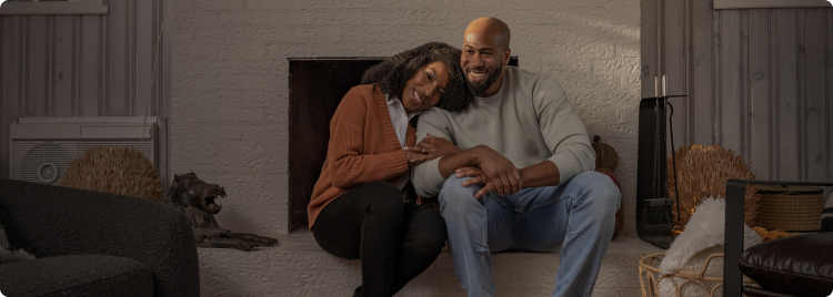 A woman hugging a man's arm with her head on his shoulder while they sit on a hearth