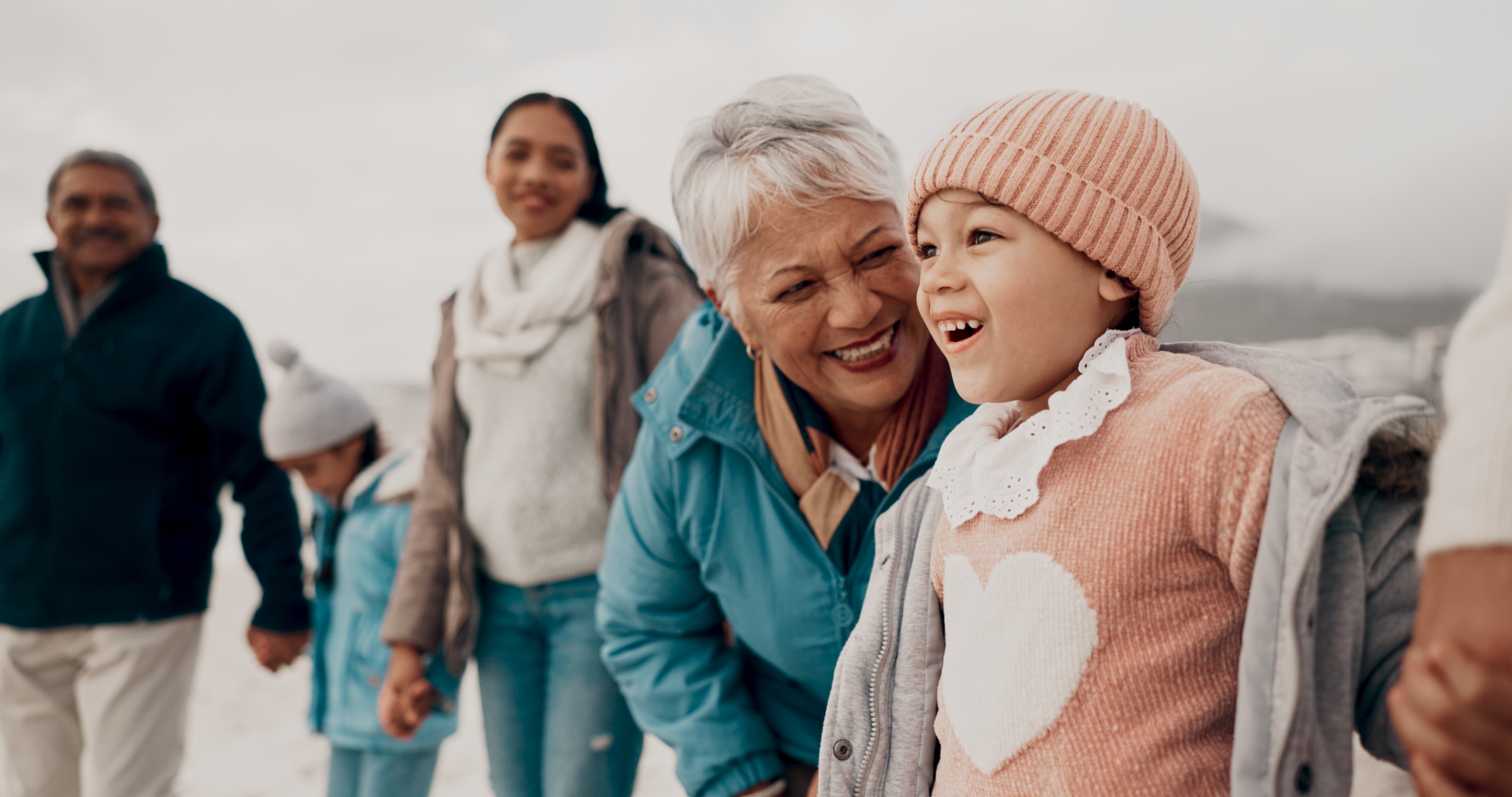 Grandparent in blue winter coat smiling with young girl in pink hat and sweater