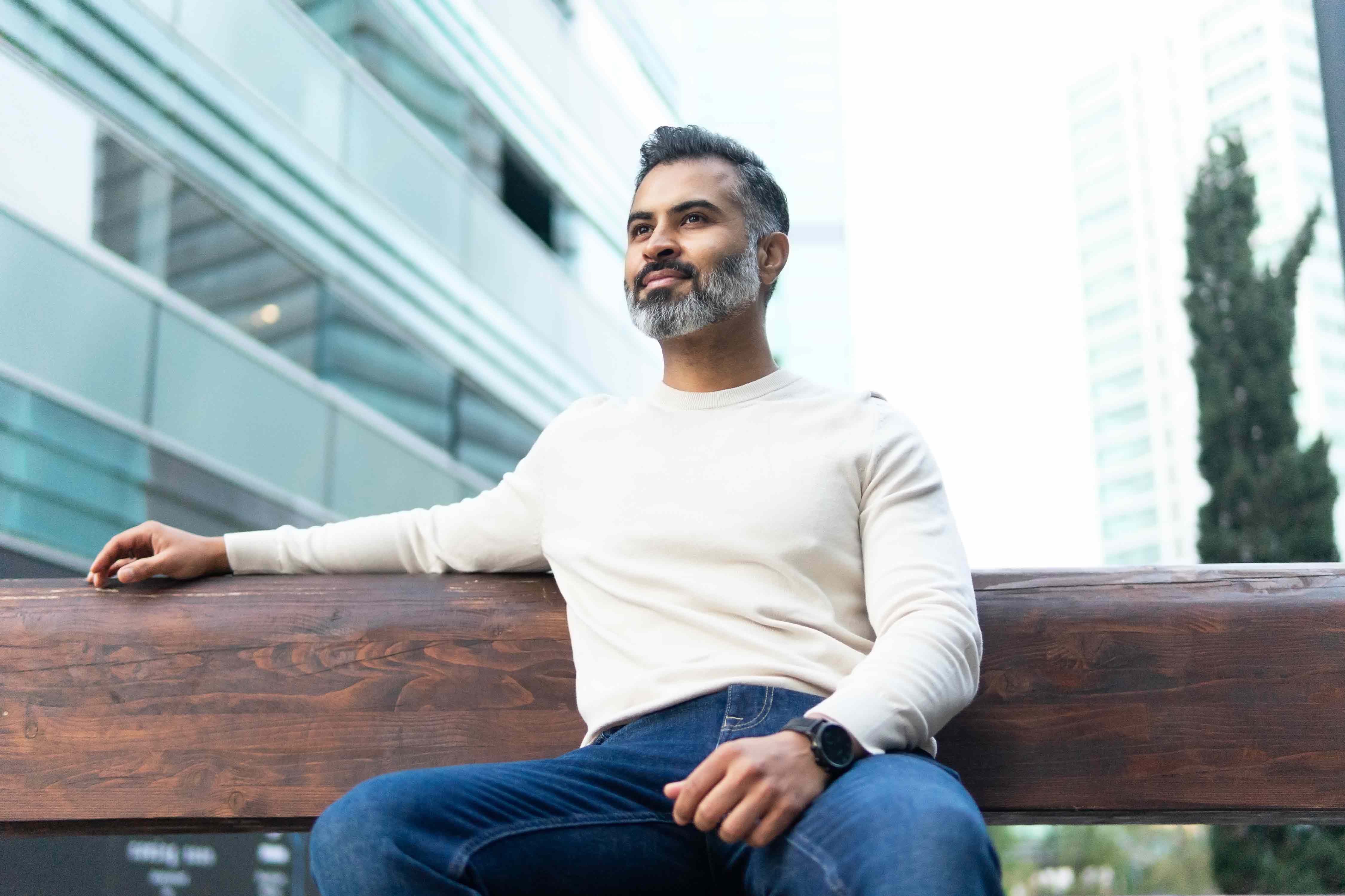 Man with salt and pepper hair sitting on a bench outside of office buildings