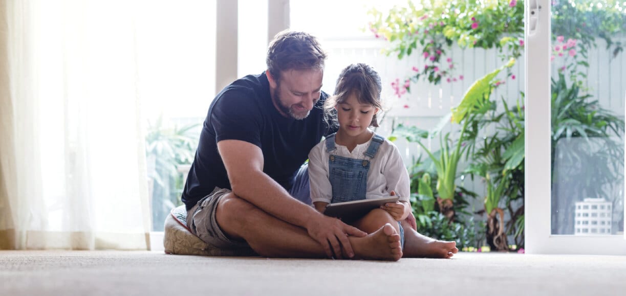 A young girl sitting with her father while they look at a tablet
