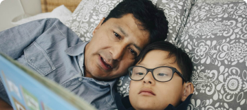 A man laying in bed with a special needs boy reading a book