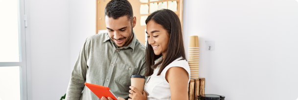 A young man and a young woman looking down at a tablet smiling