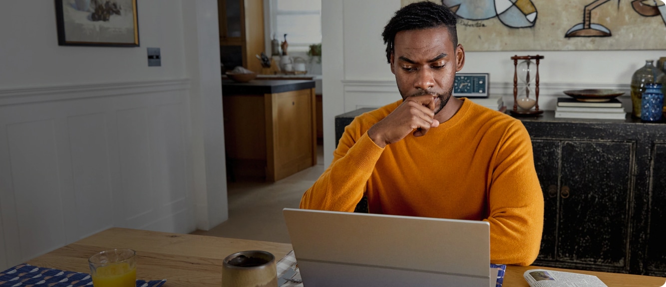 Male in orange sweater sitting at a wooden table using a laptop