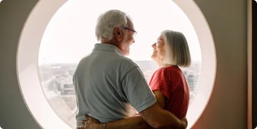A man and a woman with their arms around each other standing in front of a circular window looking at each other