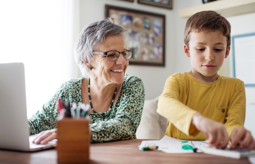 A young boy coloring while his grandmother looks on smiling