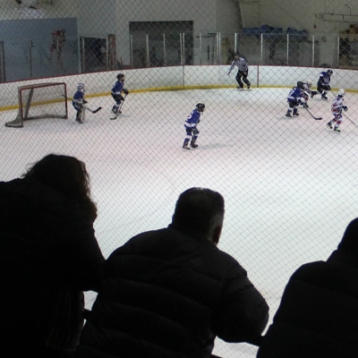 Three men standing and watching a hockey game from the stands