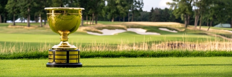 Image of a gold trophy cup standing on grass with trees in the background