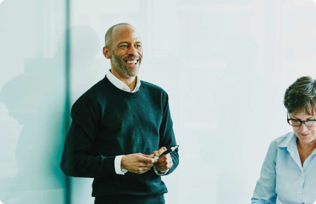 Man standing next to a white board laughing and a woman standing in front of him, looking down, smiling
