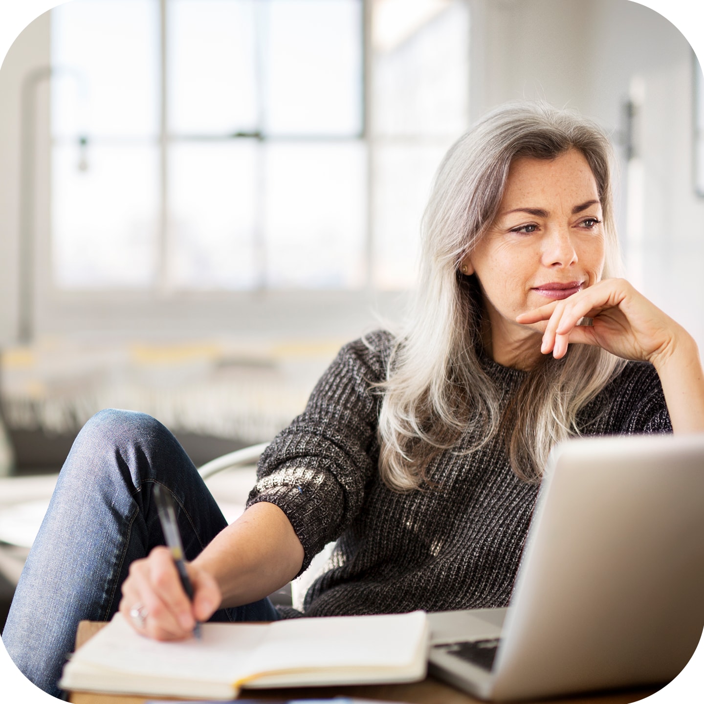 Woman sitting with laptop in front of her writing into a notebook