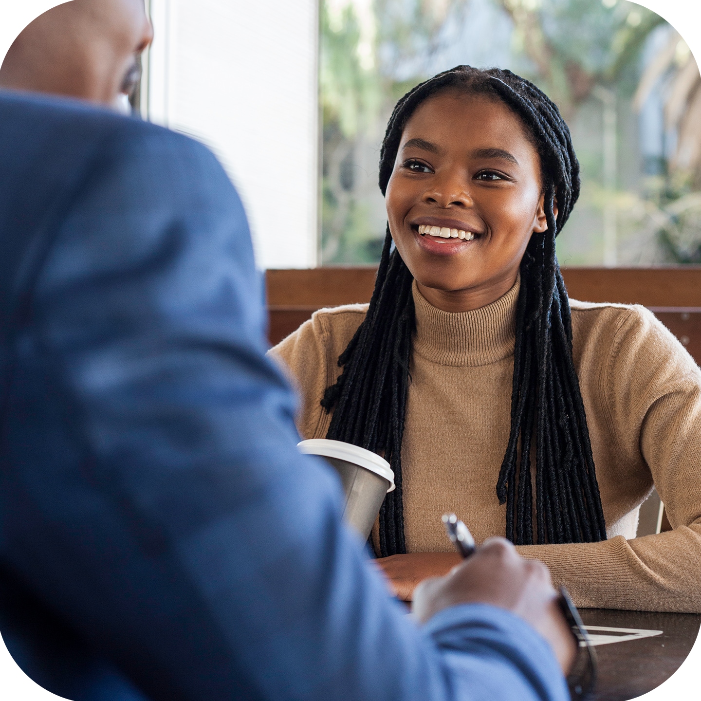 Woman in brown turtle neck top and long braided hair smiling at male in blue blazer top