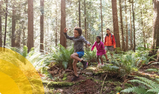 two kids running in woods with parent in orange jacket