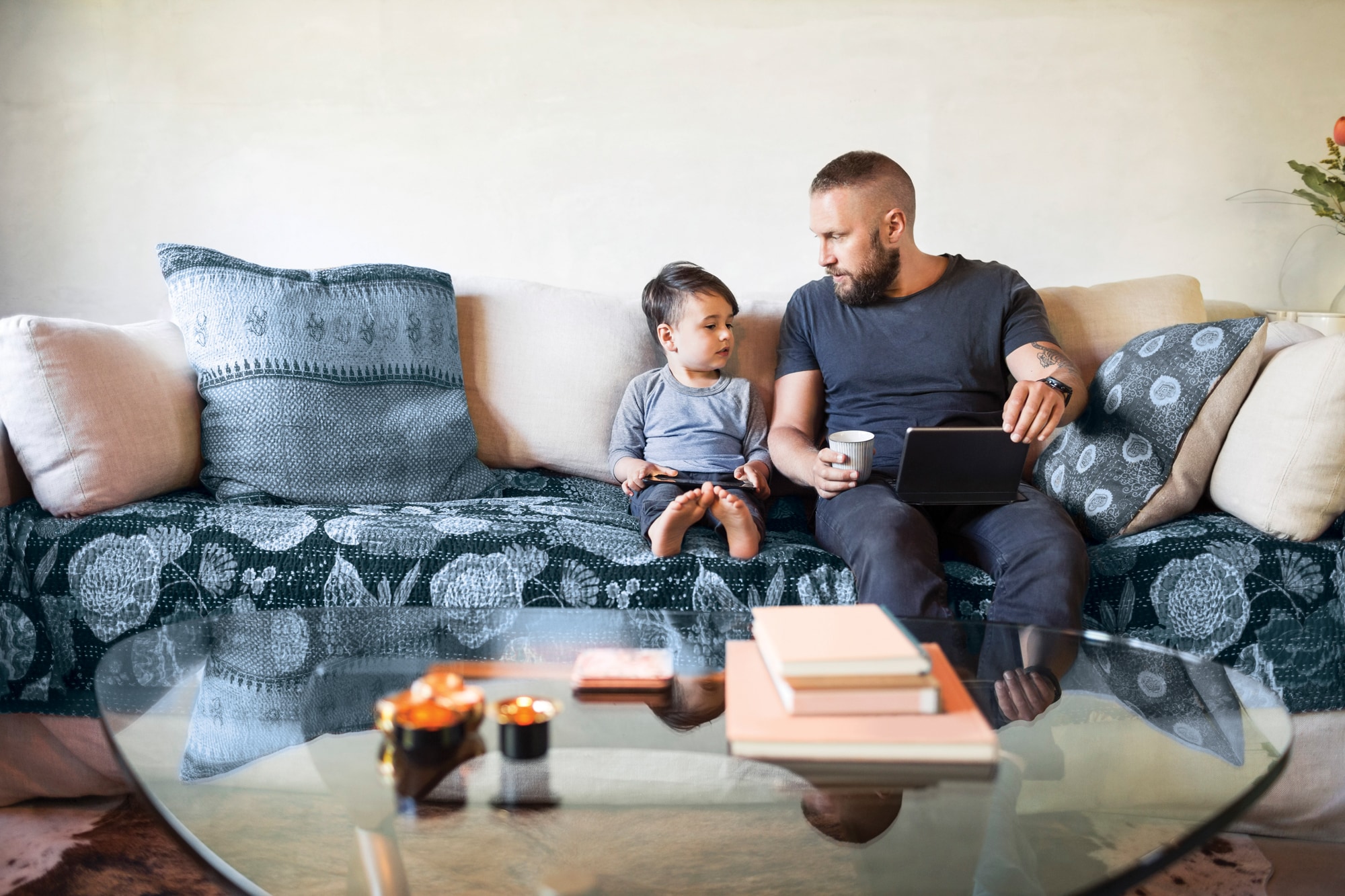 Man sitting on a couch with a little boy both holding tablets in their laps