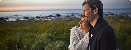 Man hugging a woman while they smile and look over the ocean