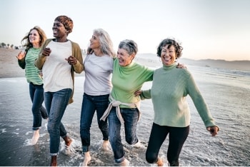 group of five woman holding one another running through the ocean water