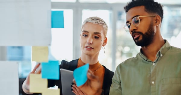 Male and female sorting sticky notes on a wall in an office